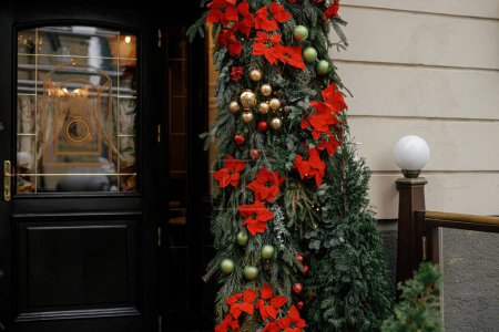 Téléchargez les photos : Branches élégantes de sapin de Noël avec des boules et poinsettia sur l'extérieur du bâtiment. Décor de Noël moderne dans la rue de la ville, fleur étoile de Noël. Vacances d'hiver en Europe. Joyeux Noël - en image libre de droit