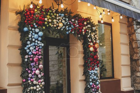 Photo for Stylish christmas fir branches with many colorful baubles on building exterior. Modern christmas decor in city street. Winter holidays in Europe. Merry Christmas - Royalty Free Image
