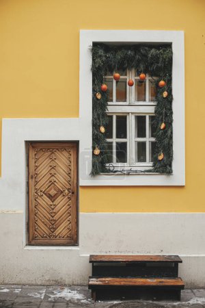 Photo for Stylish christmas branches with oranges and tangerines on white window of yellow building. Modern simple eco christmas decor in city street. Winter holidays in Europe. Merry Christmas - Royalty Free Image