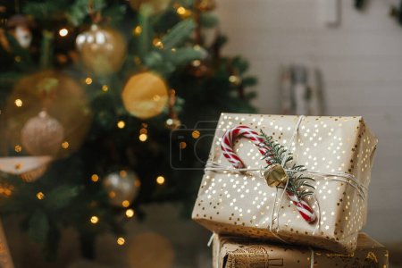 Téléchargez les photos : Joyeux Noël ! Cadeaux de Noël élégants à l'arbre de Noël avec des lumières dorées bokeh. Cadeaux de Noël enveloppés avec canne à bonbons sous arbre décoré dans la chambre. Veille atmosphérique. Bannière vacances - en image libre de droit