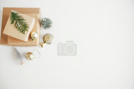 Photo for Merry Christmas! Stylish eco christmas gift boxes on white table flat lay. Simple craft christmas presents with golden baubles, bell and fir branch on rustic wood. Zero waste. Space for text - Royalty Free Image