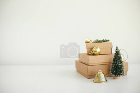 Photo for Stylish eco christmas gift boxes on white table. Simple craft christmas presents with golden baubles, tree and fir branch on rustic wood. Merry Christmas! Eco friendly holiday banner - Royalty Free Image