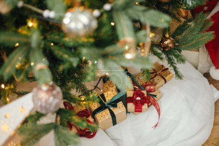 Foto de Elegantes regalos de Navidad bajo el árbol de Navidad con luces doradas. La Navidad envuelta presenta en papel dorado con cintas rojas y verdes en la habitación moderna festiva. Feliz Navidad y Felices Fiestas - Imagen libre de derechos