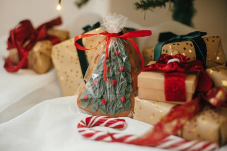 Foto de Elegantes regalos de Navidad con galleta y bastón de caramelo bajo el árbol de Navidad con luces doradas. La Navidad envuelta presenta en papel dorado con cintas rojas y verdes en la habitación festiva. Feliz Navidad. - Imagen libre de derechos