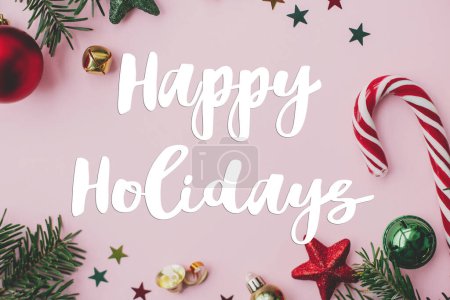 Photo for Happy Holidays text sign on christmas festive decorations, confetti, fir branches frame on pink background flat lay. Season's greeting card. Christmas postcard - Royalty Free Image
