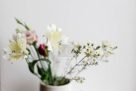 Téléchargez les photos : Bouquet élégant dans un vase en céramique à la fenêtre, image lunatique. Belles fleurs fraîches, manuka, alstroemeria, eustoma, arrangement floral d'eucalyptus. Printemps bouquet moderne gros plan - en image libre de droit