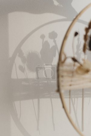 Foto de Sombra de elegante corona de otoño boho con flores secas en la pared blanca a la luz de la noche. Arreglo floral moderno y decoración creativa hecha a mano. Auténtica imagen malhumorada - Imagen libre de derechos