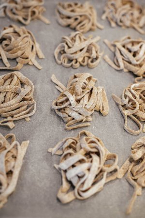 Téléchargez les photos : Homemade pasta. Dry fettuccine noodles in nests on baking tray close up. Making whole-grain pasta in kitchen, home made italian dinner - en image libre de droit