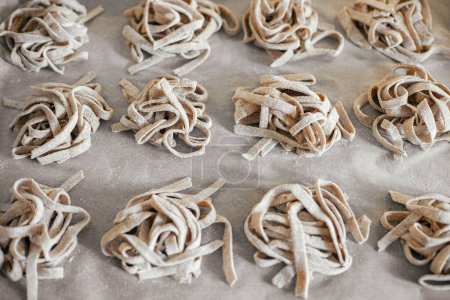 Foto de Homemade pasta. Dry fettuccine noodles in nests on baking tray close up. Making whole-grain pasta in kitchen, home made italian dinner - Imagen libre de derechos