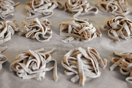 Photo for Homemade pasta. Dry fettuccine noodles in nests on baking tray close up. Making whole-grain pasta in kitchen, home made italian dinner - Royalty Free Image