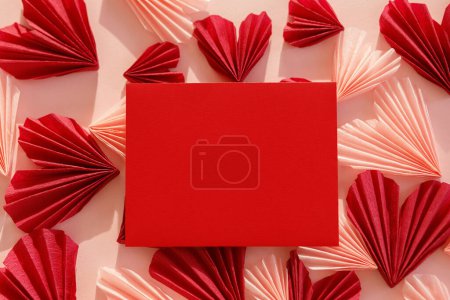 Foto de Stylish empty red card and pink and red hearts flat lay on pink paper background. Modern valentine card  mock up with heart cutouts. Love letter. Happy Valentine's day! Creative composition - Imagen libre de derechos