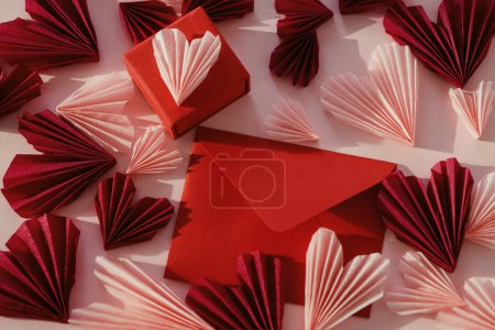 Téléchargez les photos : Happy Valentine's day! Stylish red envelope with pink hearts and gift flat lay on pink paper background. Modern valentine card with heart cutouts. Love letter. Creative composition - en image libre de droit