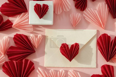 Téléchargez les photos : Happy Valentine's day! Stylish envelope with pink and red hearts and gift flat lay on pink paper background. Modern valentine card with heart cutouts. Love letter. Creative composition - en image libre de droit