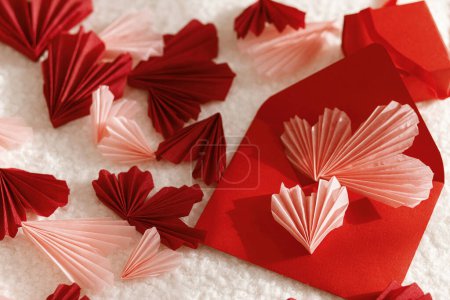 Foto de Happy Valentine's day! Stylish red envelope with pink hearts and gift on cozy soft fabric in sunlight. Modern valentine card with heart cutouts. Love letter. Creative composition - Imagen libre de derechos