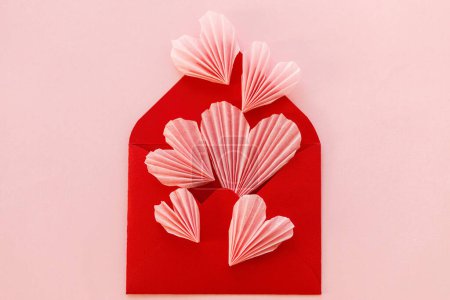 Téléchargez les photos : Happy Valentine's day! Stylish red envelope with pink hearts flat lay on pink paper background. Modern valentine heart cutouts. Love letter, space for text. Creative composition - en image libre de droit