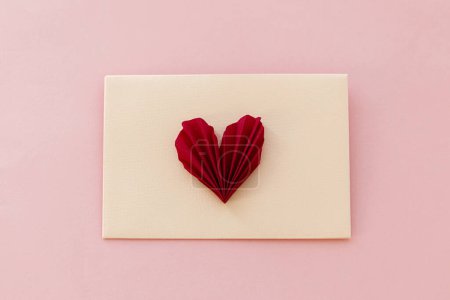 Téléchargez les photos : Stylish envelope with red heart flat lay on pink paper background. Modern valentine card, space for text. Happy Valentine's day! Love banner. Creative letter composition - en image libre de droit
