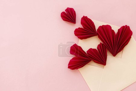 Téléchargez les photos : Stylish envelope with red hearts flat lay on pink paper background. Modern valentine card, space for text. Happy Valentine's day! Love banner. Creative letter composition - en image libre de droit