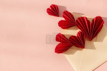 Téléchargez les photos : Happy Valentine's day! Stylish envelope with red hearts flat lay on pink paper background. Modern valentine card, space for text. Love banner. Creative letter composition - en image libre de droit