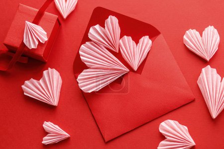 Photo for Happy Valentine's day! Stylish red envelope with pink hearts and gift flat lay on red paper background. Modern valentine card with heart cutouts. Love letter. Creative composition - Royalty Free Image