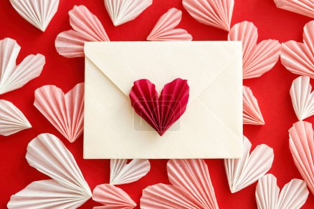 Téléchargez les photos : Valentines day flat lay. Stylish envelope with pink and red hearts composition on red paper background. Creative modern valentine hearts cutouts. Happy Valentine's day! Love letter - en image libre de droit