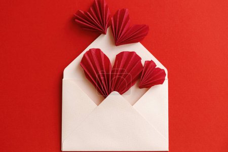 Téléchargez les photos : Happy Valentine's day! Stylish envelope with pink and red hearts composition on red paper background. Creative modern flat lay with valentine hearts cutouts. Love letter - en image libre de droit