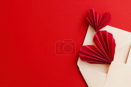 Foto de Happy Valentine's day! Stylish envelope with red hearts flat lay on red paper background. Modern valentine card with space for text. Love letter. Creative composition - Imagen libre de derechos