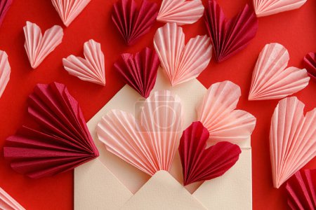 Téléchargez les photos : Happy Valentine's day! Stylish envelope with pink and red hearts flat lay on red paper background. Creative modern composition with valentine hearts cutouts. Love letter - en image libre de droit
