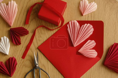 Foto de Stylish envelope with pink hearts, scissors and gift box on rustic wooden table top view. Valentine day holiday preparations. Modern creative love letter. Happy Valentine's day! - Imagen libre de derechos