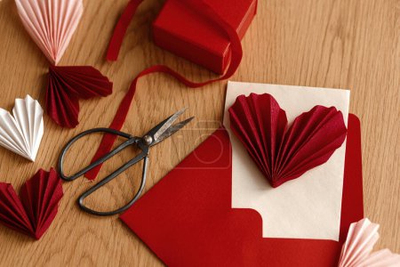 Foto de Happy Valentine's day! Stylish envelope with red heart, scissors and gift box on rustic wooden table top view. Modern cute valentine heart cutouts, holiday preparations. Creative love letter - Imagen libre de derechos