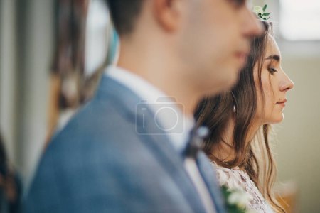 Foto de Stylish bride and groom standing during holy matrimony in church. Wedding ceremony in cathedral. Classic spiritual wedding couple with burning modern candles - Imagen libre de derechos