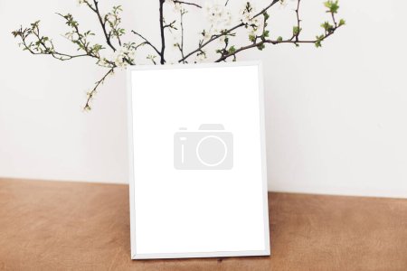 Foto de Photo frame mockup and blooming cherry branches on wooden table against white wall. Empty picture frame template and spring flowers. Simple countryside living. Space for text - Imagen libre de derechos
