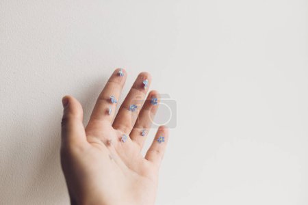 Photo for Cute little blue flowers on hand and fingers against white wall. Delicate forget me not petals on palm. Simple aesthetic image. Hello spring. Skin care and organic cosmetics concept - Royalty Free Image