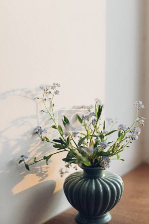 Photo for Beautiful little blue flowers in vase in warm evening sunlight on rustic wooden table. Delicate myosotis petals, forget me not spring flowers. Simple countryside living, home decor - Royalty Free Image