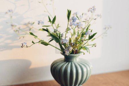 Photo for Beautiful little blue flowers in vase in warm sunlight on rustic wooden background. Delicate myosotis petals, forget me not spring flowers. Atmospheric evening moment. Simple countryside living - Royalty Free Image