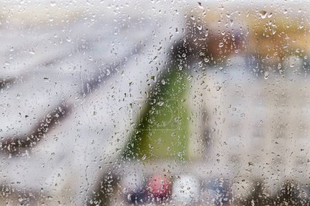 Foto de Raindrops on window background. Water droplets on glass surface. Rainy weather. Rain drops on background of city buildings. Rainy day wallpaper - Imagen libre de derechos