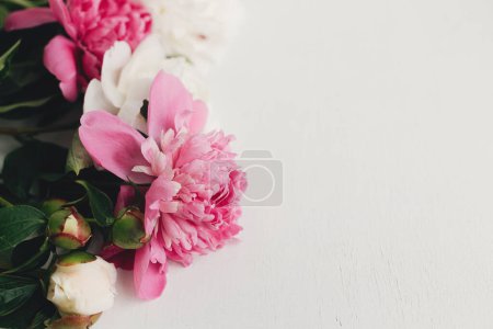 Téléchargez les photos : Beautiful peonies on rustic white wood, space for text. Stylish floral greeting card template. Fresh pink and white peony flowers border on wooden background, moody banner - en image libre de droit