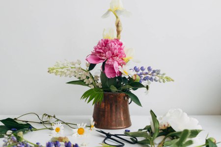 Photo for Modern summer flowers still life arrangement in vintage vase on white wood. Creative floral image. Stylish peony, lupin, iris and daisy composition and scissors on rustic table - Royalty Free Image