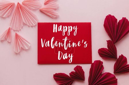 Téléchargez les photos : Happy valentines day text on red card and stylish hearts flat lay on pink paper background. Love letter concept. Valentines day greeting card. - en image libre de droit