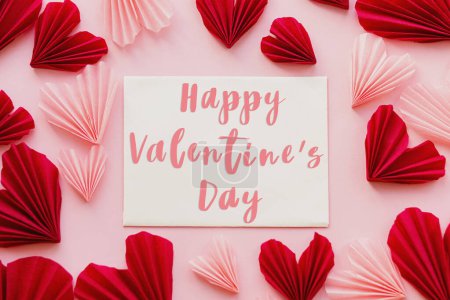 Téléchargez les photos : Happy valentines day text on card and stylish red and pink hearts flat lay on pink paper background. Modern Valentines day greeting card. Handwritten sign, love letter - en image libre de droit