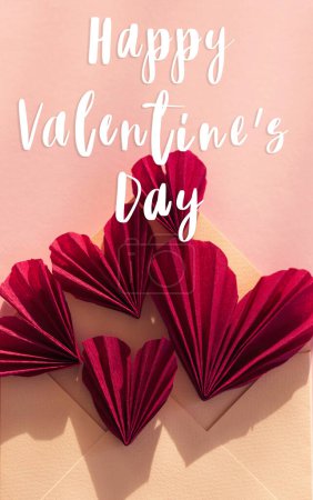 Téléchargez les photos : Happy valentines day text on stylish envelope with red hearts flat lay on pink paper background in sunlight. Modern Valentines day greeting card. Handwritten sign, love letter - en image libre de droit