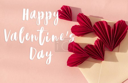 Téléchargez les photos : Happy valentines day text on stylish envelope with red hearts flat lay on pink paper background. Modern Valentines day greeting card. Handwritten sign, love letter - en image libre de droit