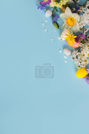 Foto de Happy Easter! Easter eggs, colorful flowers and blooming cherry petals flat lay on blue background. Stylish festive template with space for text. Greeting card or banner - Imagen libre de derechos
