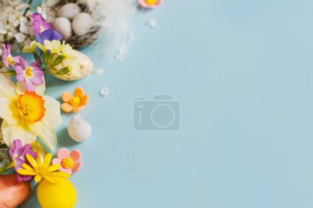 Foto de Stylish Easter eggs, colorful flowers and cherry blossoms on blue background with copy space. Happy Easter! Greeting card template. Modern holiday banner. Festive composition - Imagen libre de derechos