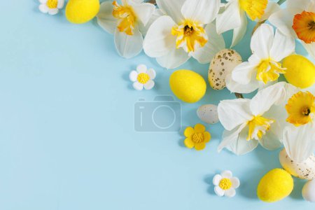 Foto de Happy Easter! Easter eggs and yellow daffodils flowers flat lay on blue background. Stylish festive template with space for text. Greeting card or banner - Imagen libre de derechos