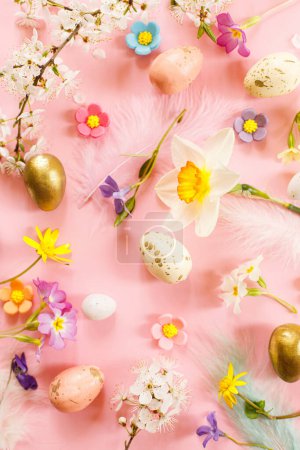 Téléchargez les photos : Stylish Easter eggs, spring flowers and feathers flat lay on pink background. Happy Easter! Greeting card template. Modern floral colorful holiday banner - en image libre de droit