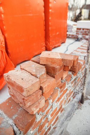 Foto de Stack of red bricks on concrete foundation, process of house building. Concrete foundation with bricks for laying. Building materials at construction site - Imagen libre de derechos