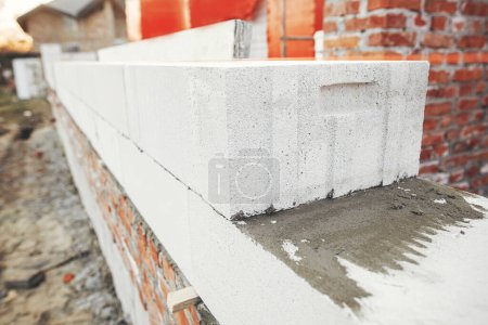Foto de Laying autoclaved aerated concrete blocks with reinforcement and adhesive. Installing white blocks close up. Masonry. Process of house building at construction site - Imagen libre de derechos
