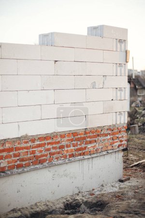 Photo for Masonry autoclaved aerated concrete blocks on bricks and concrete foundation. Laying white blocks for house wall. Process of house building at construction site. - Royalty Free Image