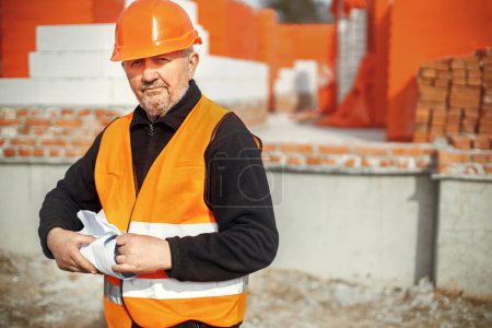 Photo for Senior male foreman in hardhat standing with blueprints at building new modern house. Portrait of man engineer or construction worker with plans at construction site. Copy space - Royalty Free Image