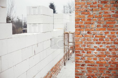 Foto de Masonry autoclaved aerated concrete blocks and bricks on concrete foundation. Laying walls with white blocks. Process of house building at construction site - Imagen libre de derechos